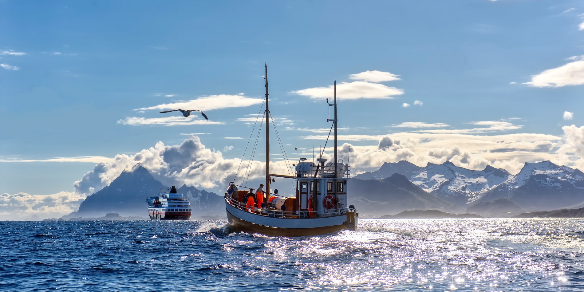 Un navire Hurtigruten naviguant à l’horizon, avec un bateau de pêche local derrière lui 