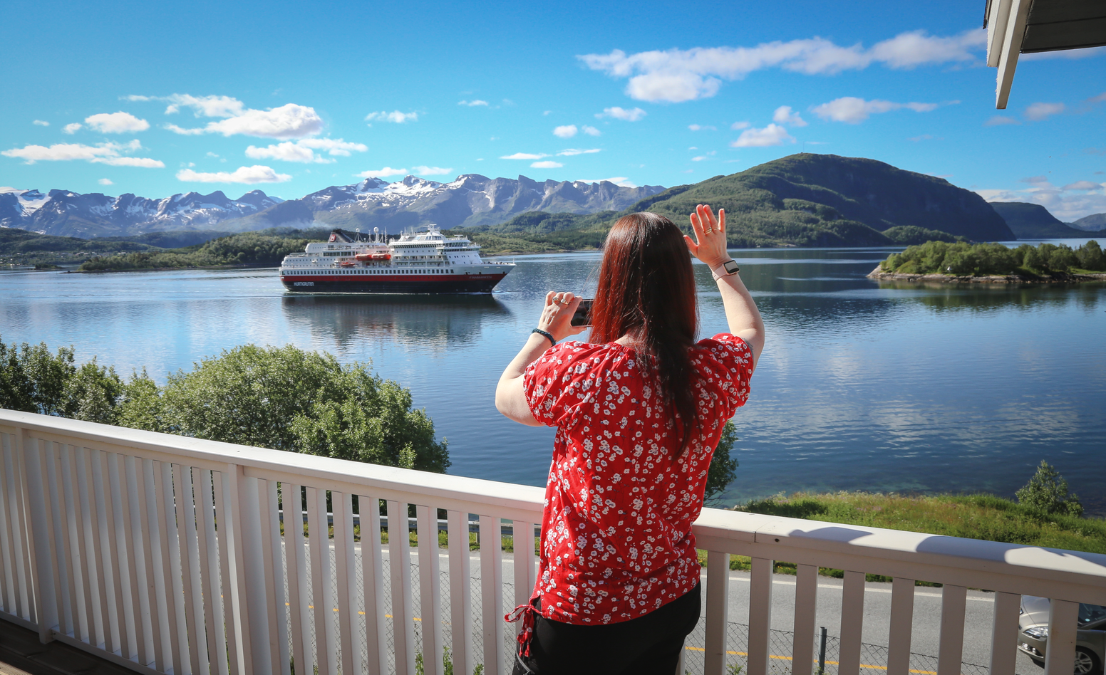 Eva Rendal devant sa maison saluant de la main le navire Hurtigruten passant devant chez elle