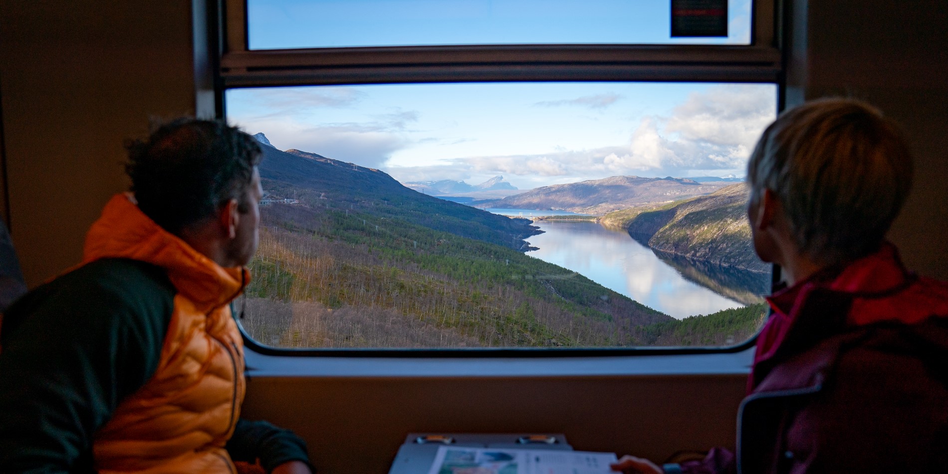 Un couple admirant la vue sur un lac depuis la fenêtre du train arctique