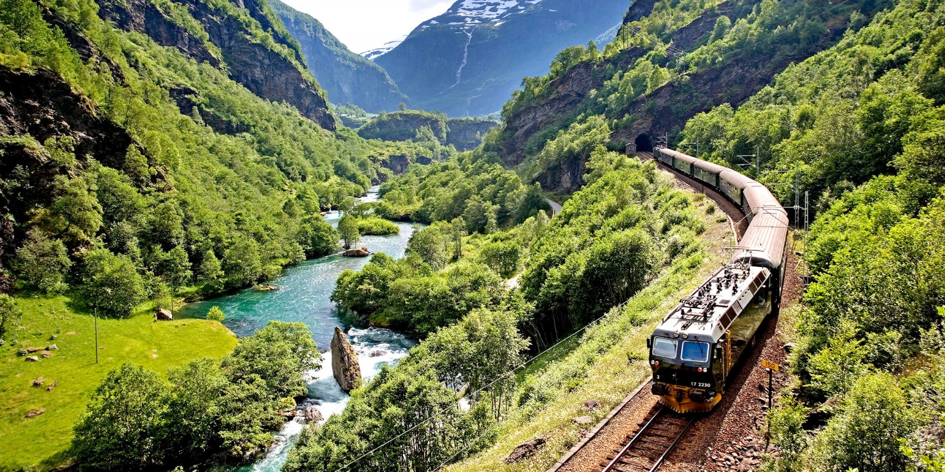 La ligne ferroviaire de Flåm lors d’une chaude journée d’été, les arbres sont verts et le fleuve bleu